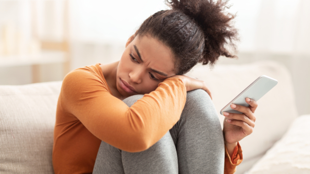 Loneliness. Sad African American Woman Holding Cellphone Having No Friends To Call Sitting On Couch At Home. Selective Focus