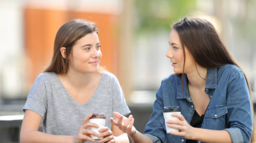 Two friends talking in a park drinking coffee